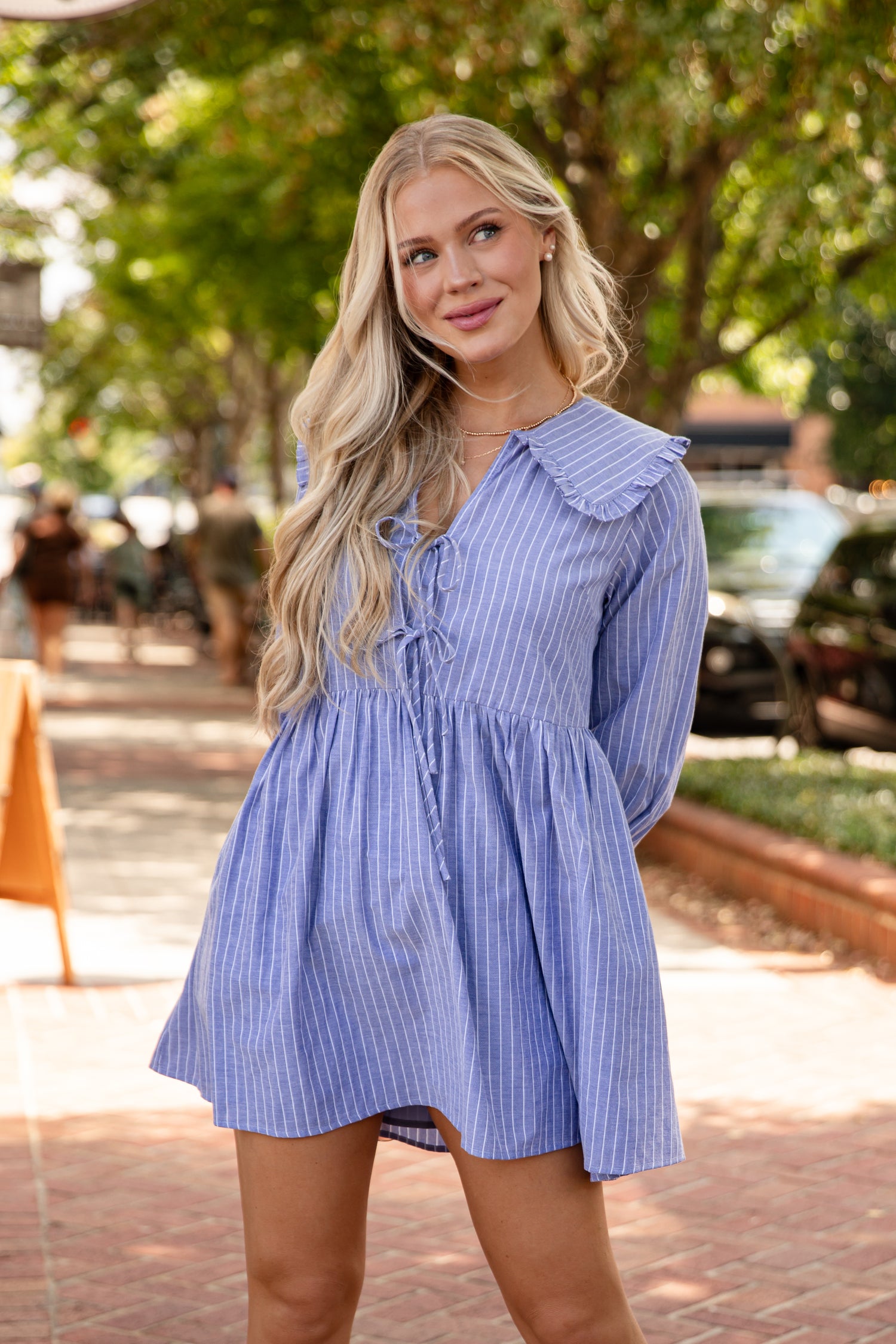 Woman wearing a blue striped dress standing outdoors with trees and people in the background