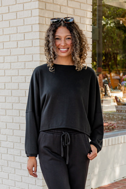 Woman wearing a black outfit standing against a brick wall.
