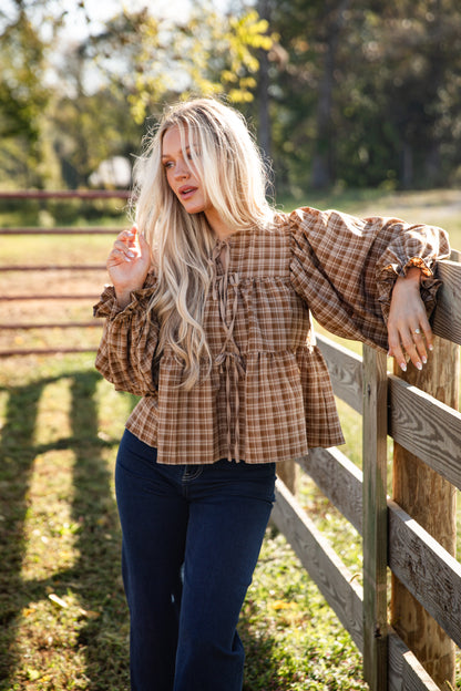 Woman wearing a plaid shirt and jeans standing by a wooden fence in a field.