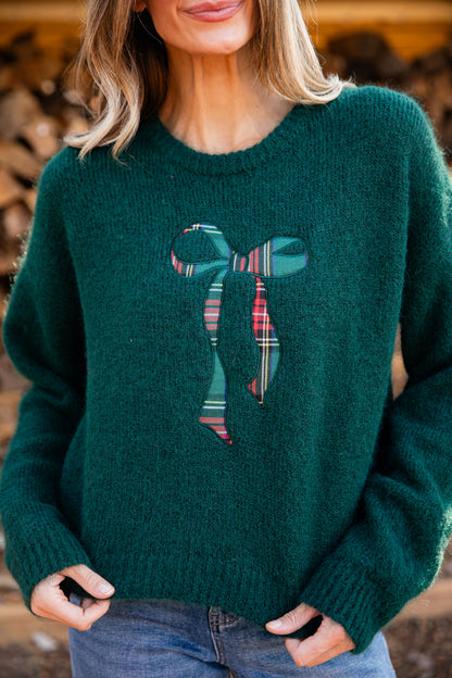 Person wearing a green sweater with a plaid bow design.