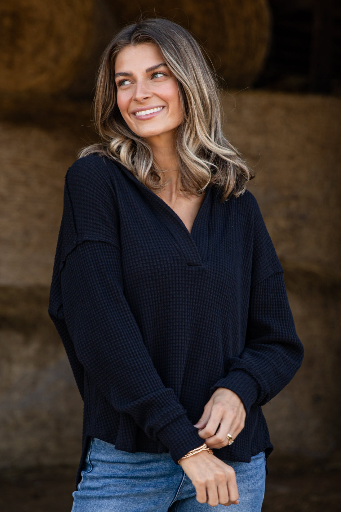 Woman wearing a black top and blue jeans standing in front of hay bales.
