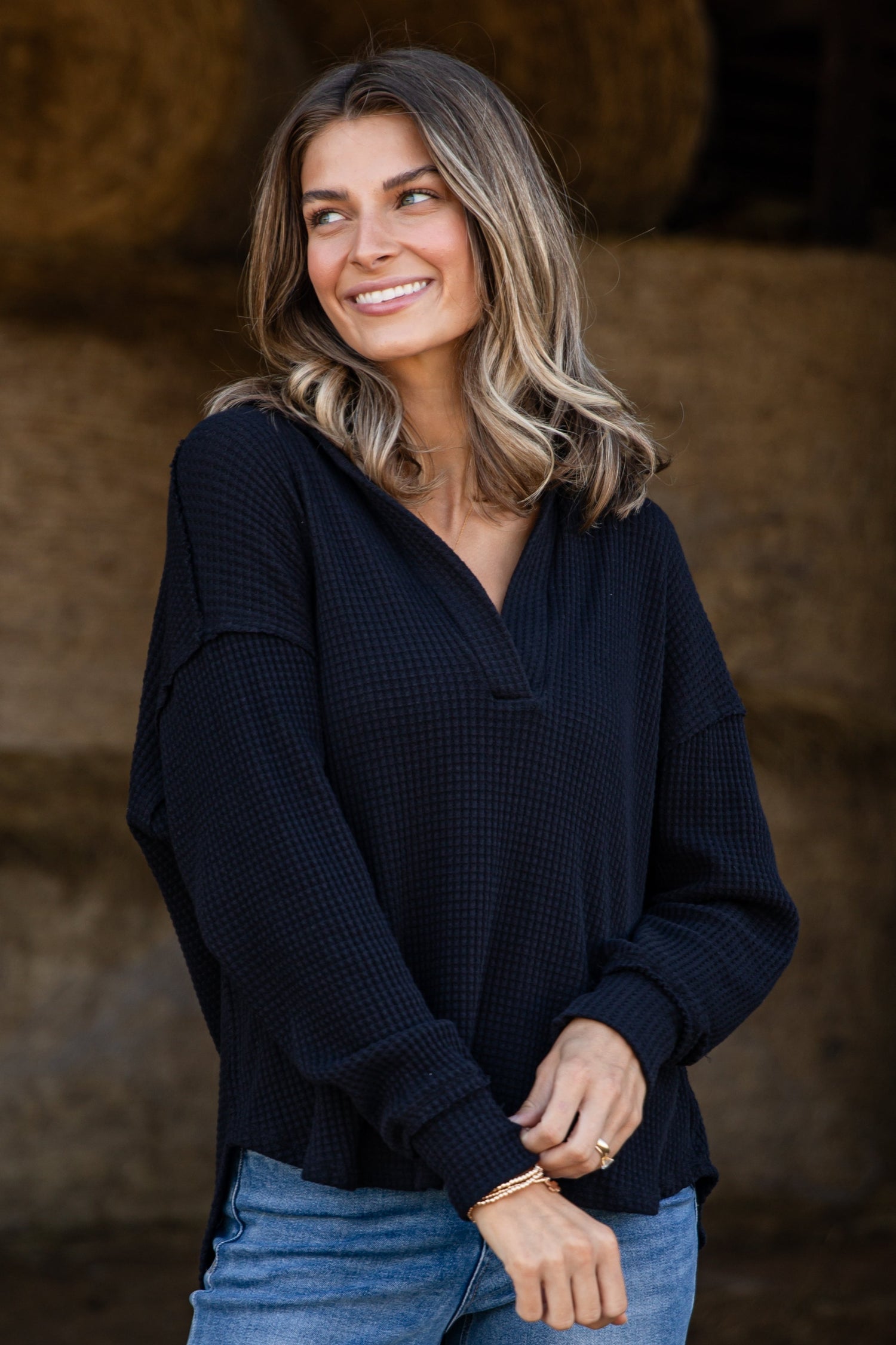 Woman wearing a black top and blue jeans standing in front of hay bales.