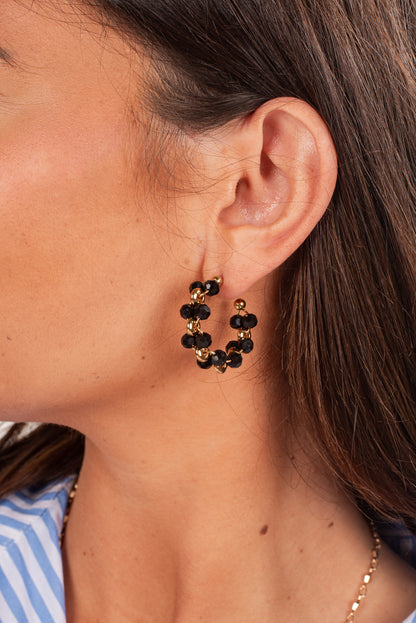 Close-up of a person wearing gold hoop earrings with black beads.