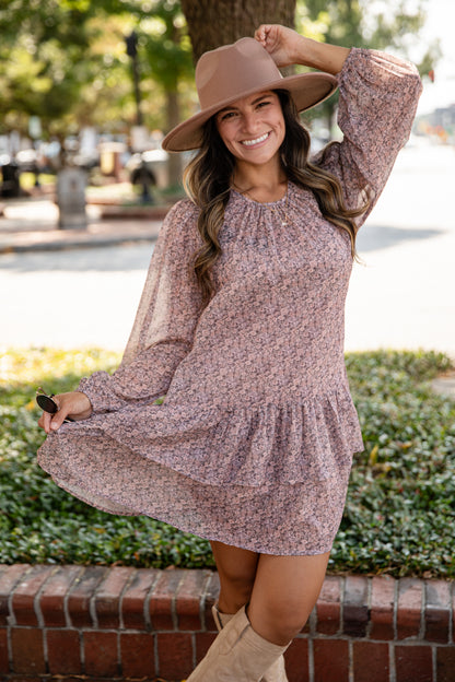 Woman in a floral dress and wide-brimmed hat standing outdoors.