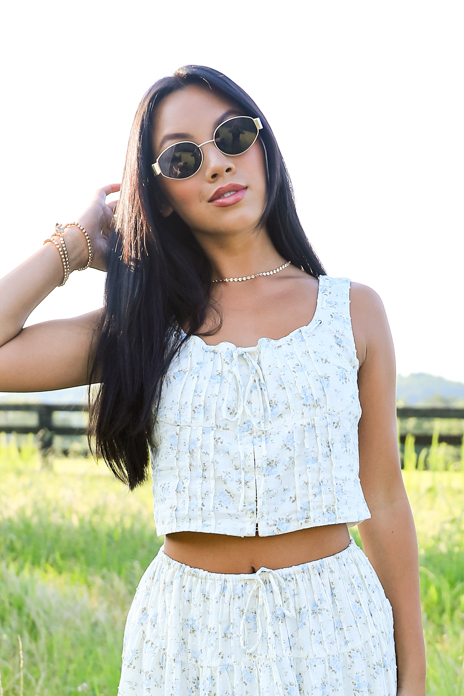 Woman wearing a light blue floral dress and sunglasses in a grassy field