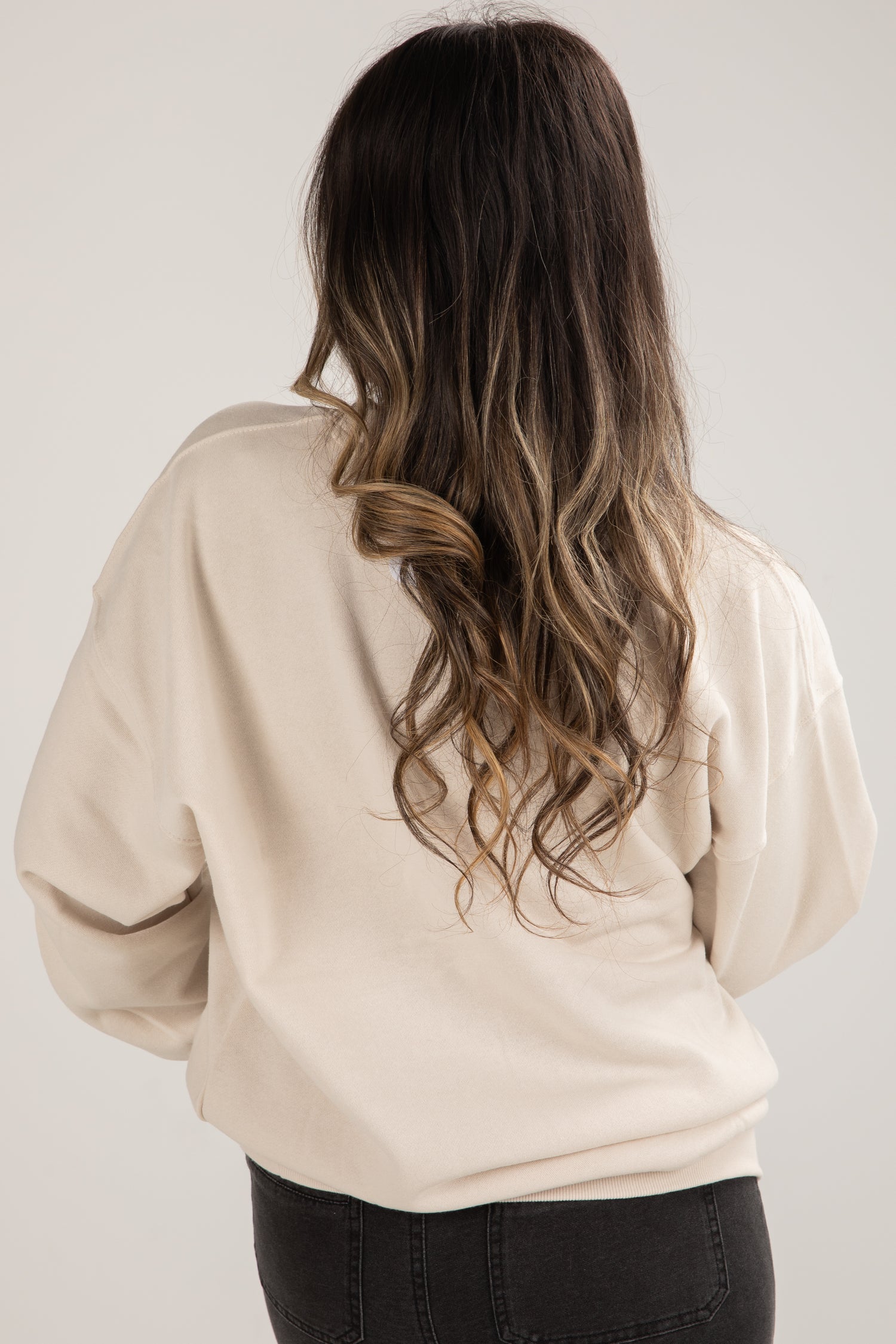 Person wearing a beige sweater with long, wavy hair on a plain background