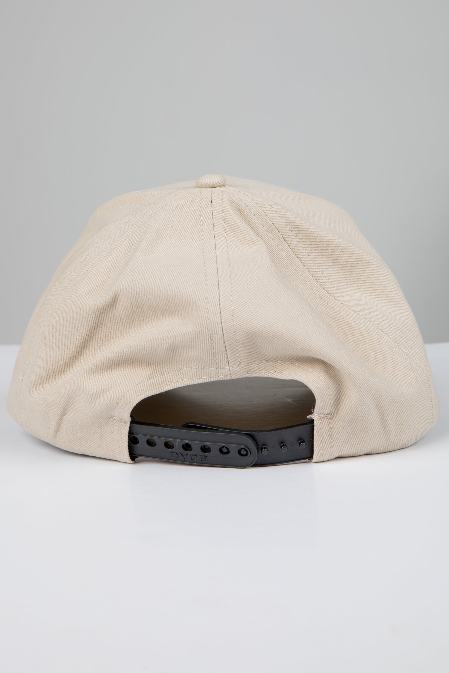 Beige cap with a black adjustable strap on a light gray background