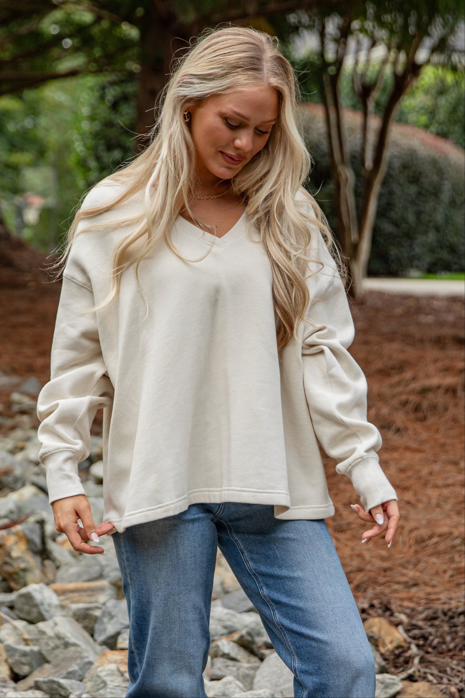Woman wearing a white sweater and blue jeans standing outdoors on a rocky path.