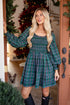 Woman in a green plaid dress standing in front of a decorated Christmas tree.