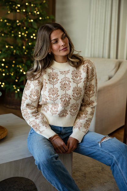 Woman wearing a patterned sweater and jeans sitting in a cozy living room with a Christmas tree.