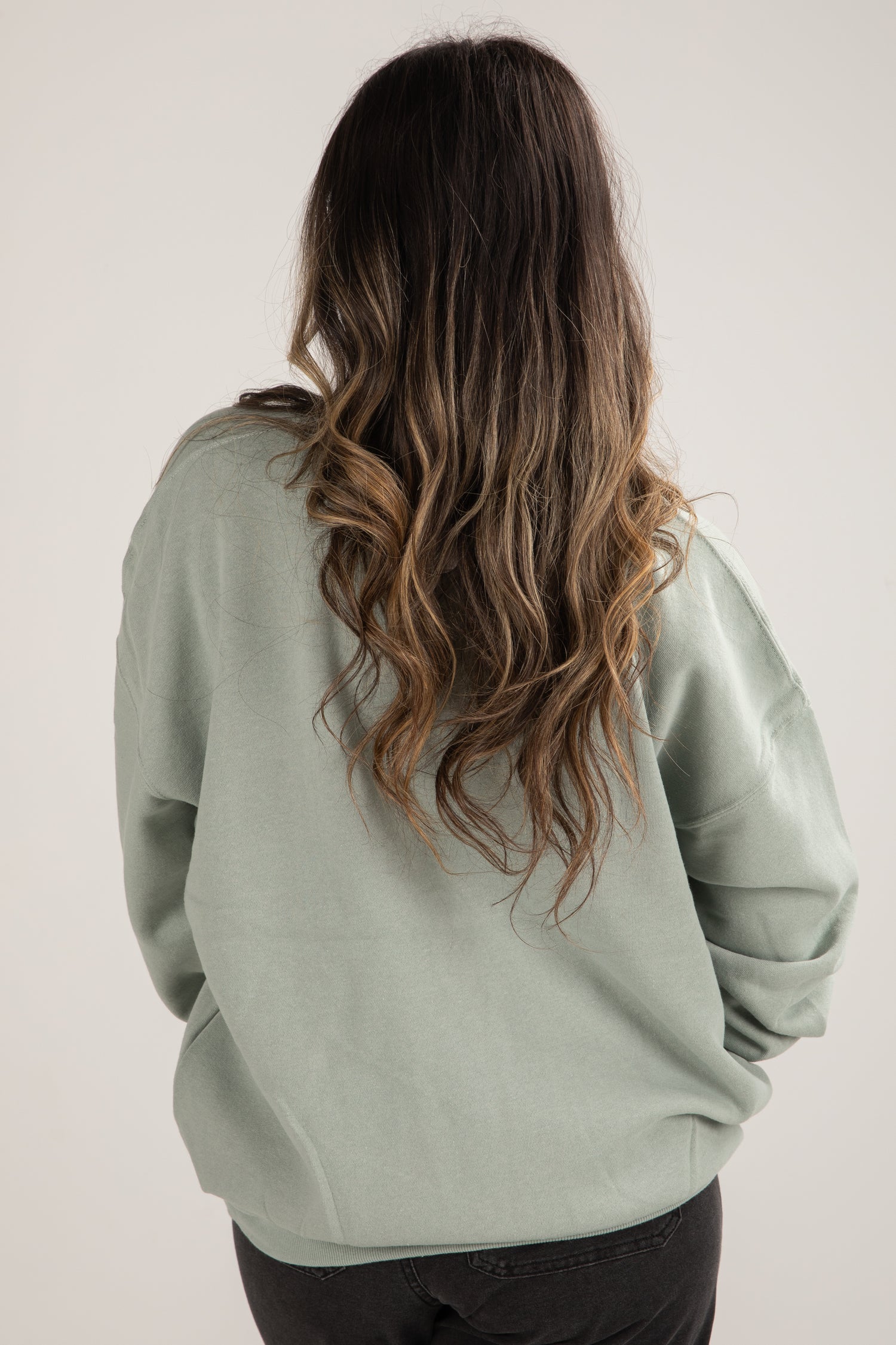 Person wearing a light green sweatshirt with long, wavy hair on a plain background