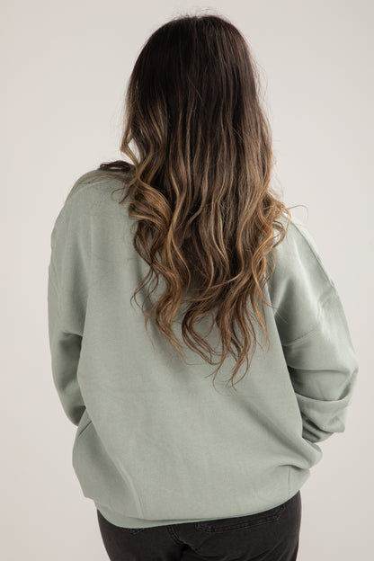 Person wearing a light green sweatshirt with long, wavy hair on a plain background