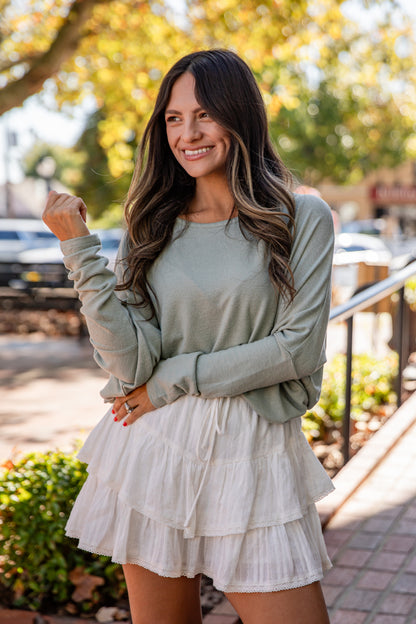 Woman wearing a light green long-sleeve top and white ruffled skirt outdoors.