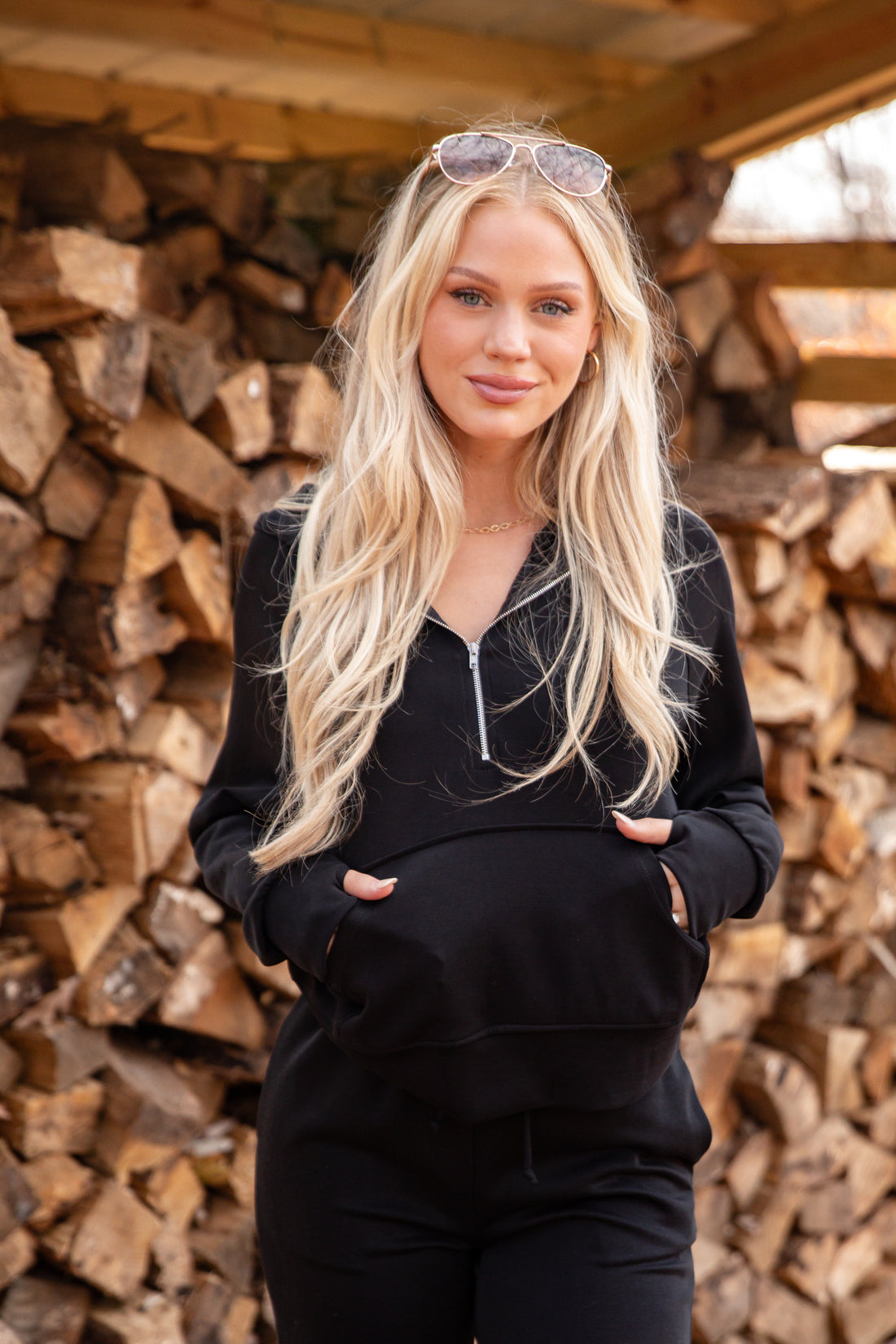 Woman in black outfit standing in front of stacked firewood