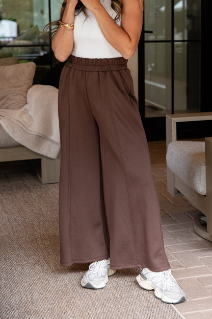Person wearing brown wide-leg pants and white sneakers in a living room setting