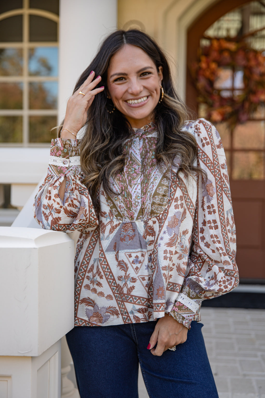 Woman wearing a patterned blouse and jeans standing in front of a house.