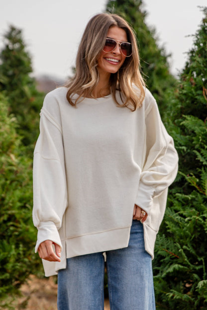 Woman in a white sweater and blue jeans standing in a field of trees