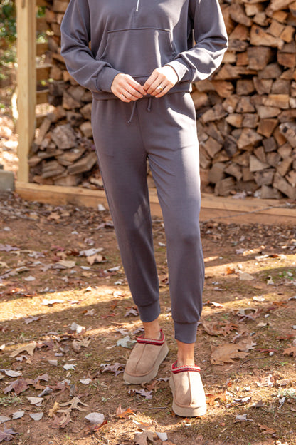 Person wearing a gray tracksuit standing in front of stacked wood.