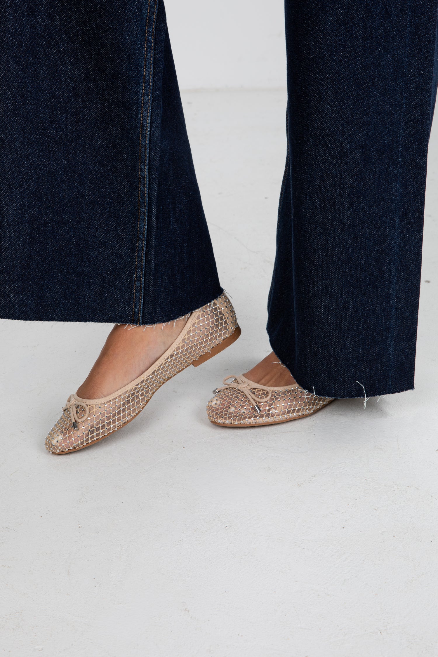 Person wearing patterned flats with dark jeans on a white background