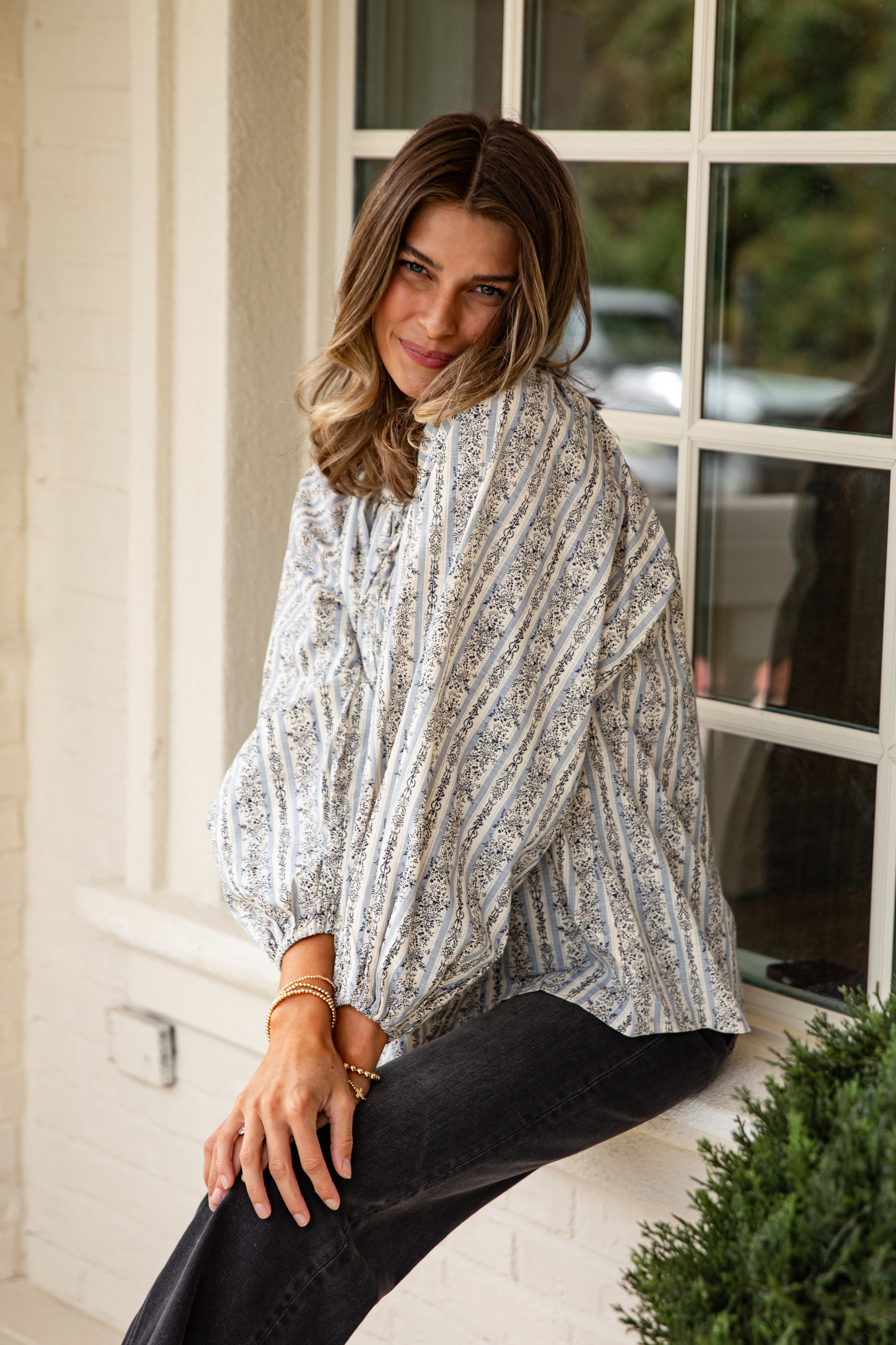 Woman wearing a patterned poncho sitting on a windowsill.