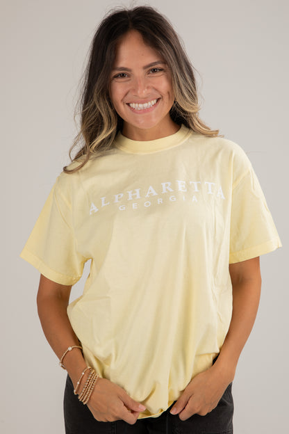 Woman wearing a light yellow t-shirt with text on a plain background