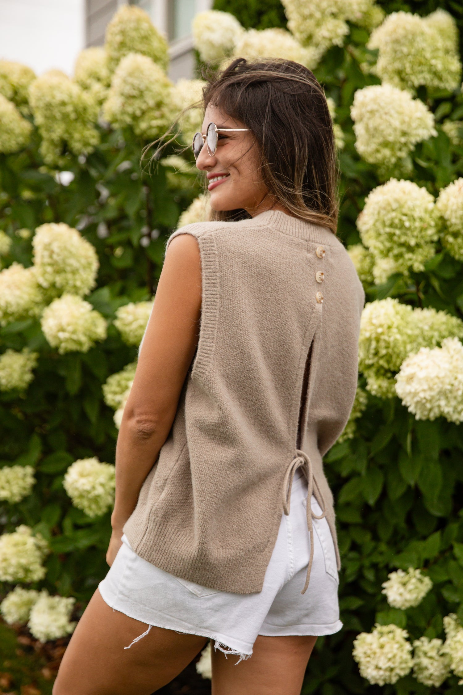 Woman wearing a beige sleeveless sweater over a white shirt with a floral background