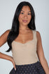 Woman wearing a beige tank top and dark pants against a plain background