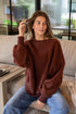 Woman wearing a brown oversized sweater sitting on a couch indoors.