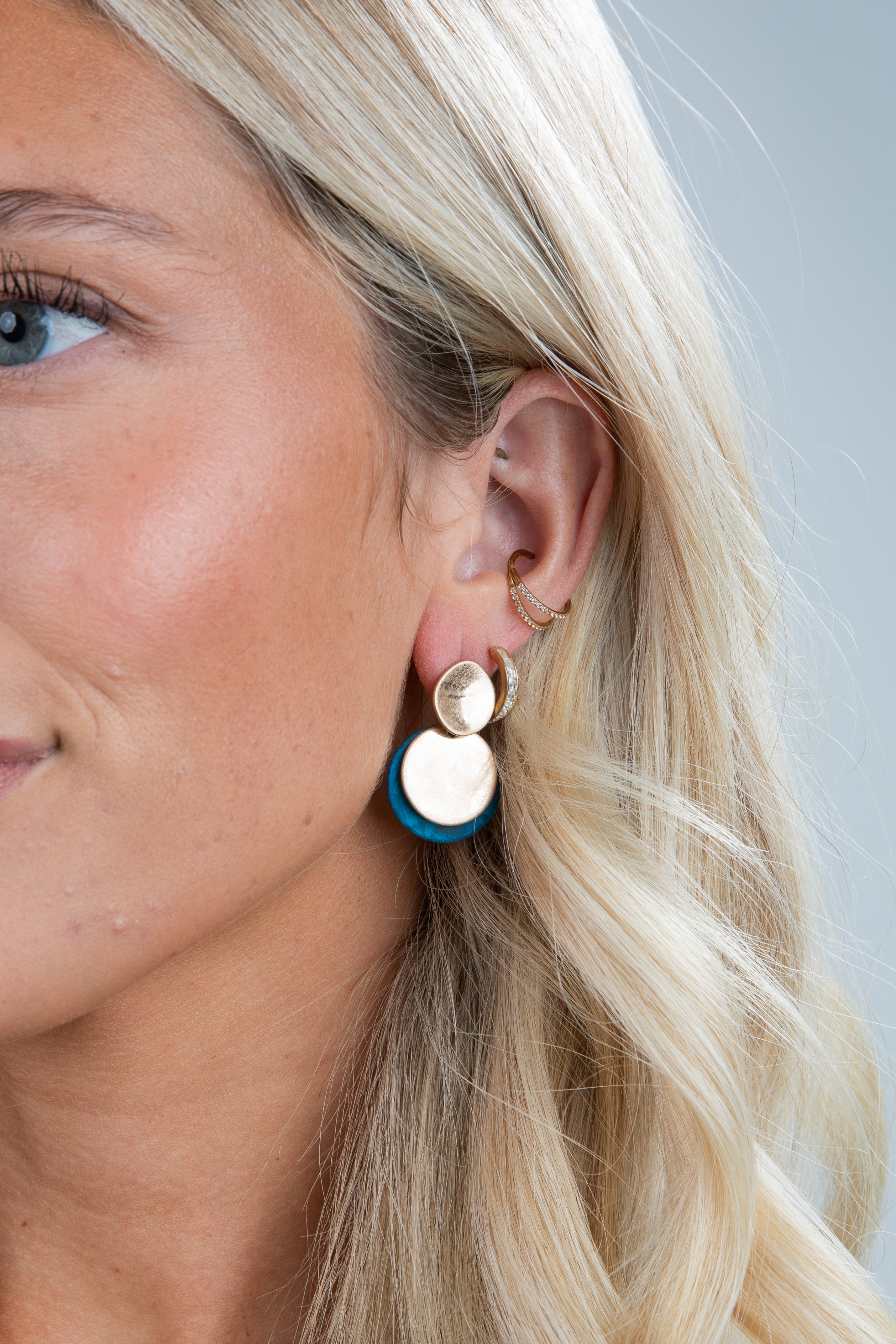 Close-up of a woman wearing gold and blue earrings with a neutral background