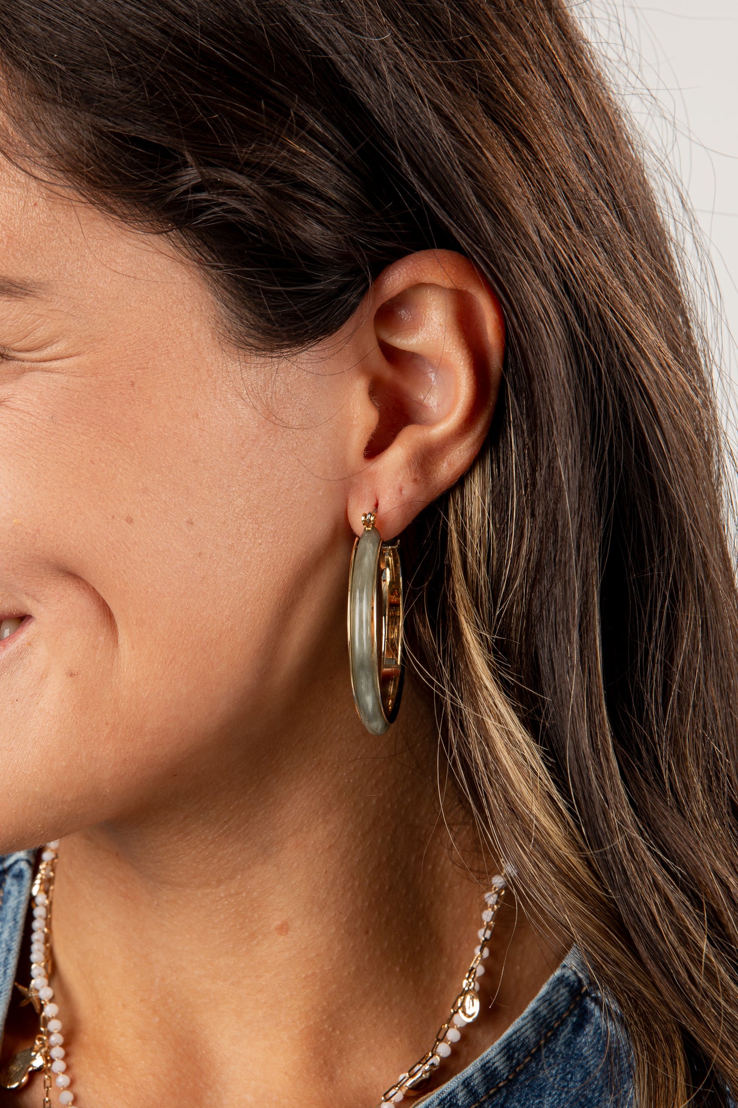 Close-up of a person wearing gold hoop earrings with a neutral background