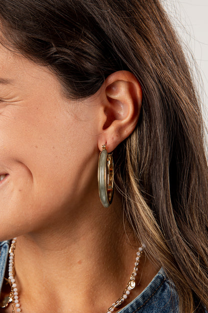 Close-up of a person wearing gold hoop earrings with a neutral background