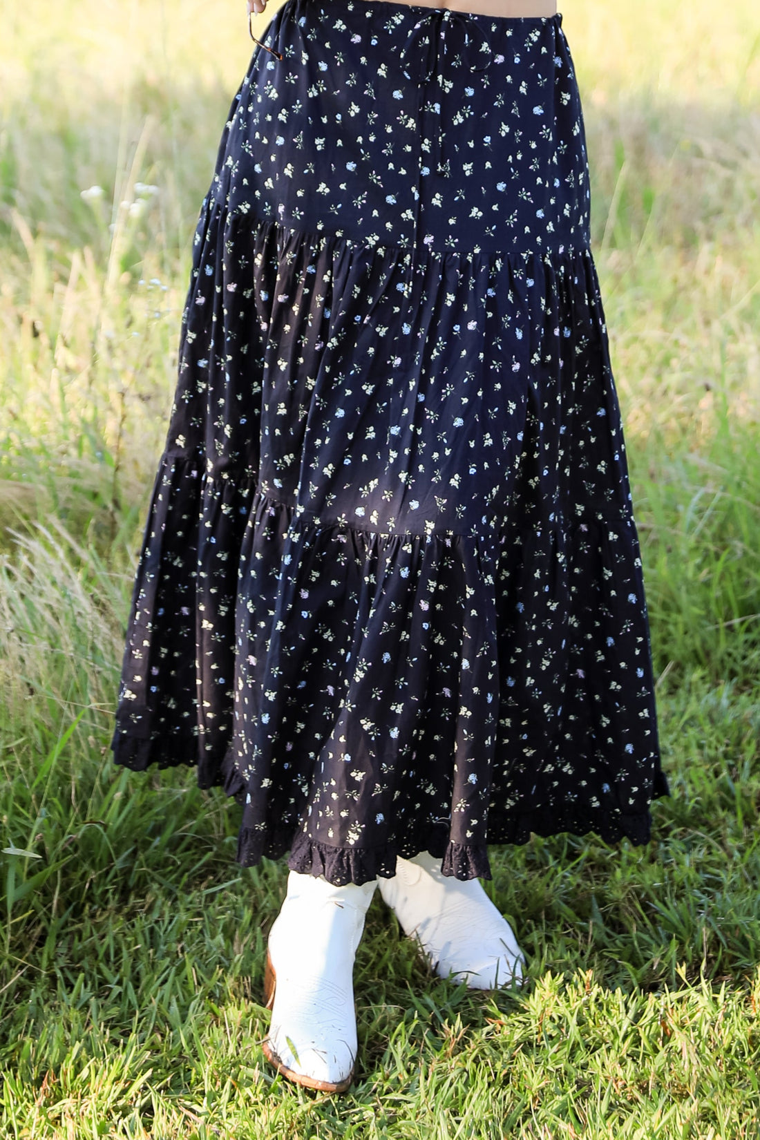 Woman wearing a black polka dot dress standing in a grassy field with mountains in the background