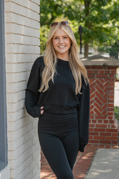 Woman in black outfit standing against a brick wall outdoors