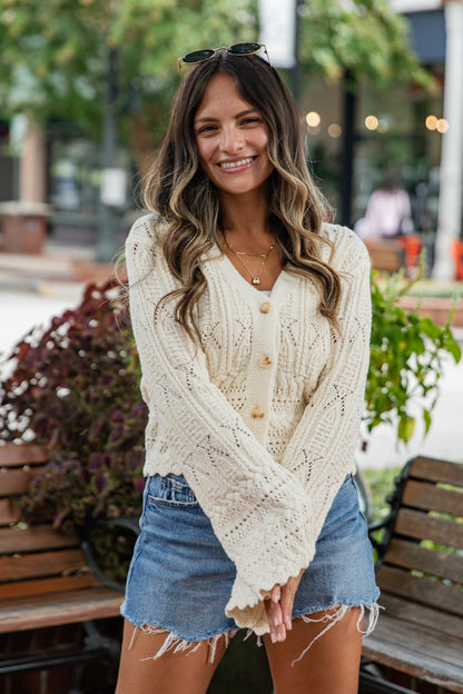 Woman wearing a cream cardigan and denim shorts outdoors