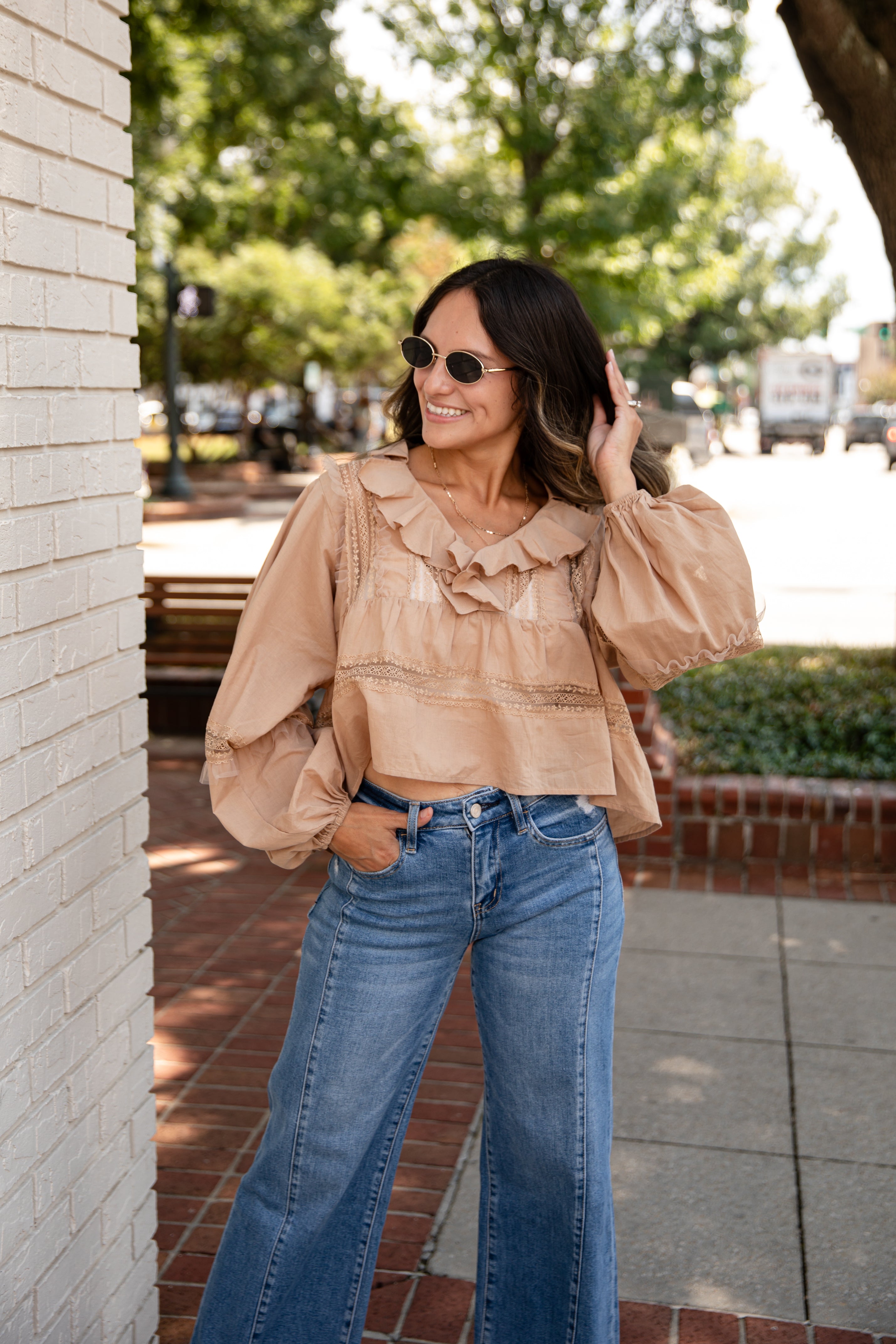Woman wearing a beige blouse with ruffles and blue jeans standing outdoors.