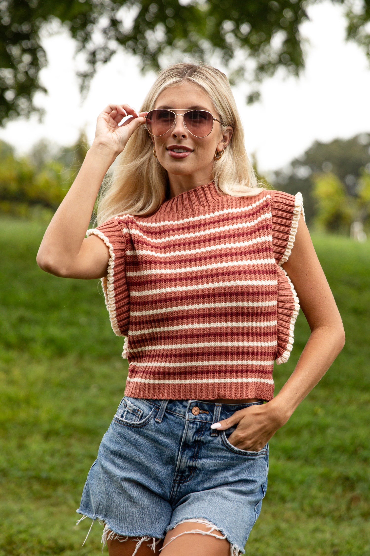Woman wearing a striped sleeveless top and denim shorts outdoors.