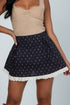 Woman wearing a navy blue patterned skirt with white lace trim on a plain background