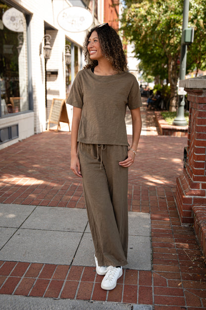 Woman in a brown outfit standing on a sidewalk with shops in the background
