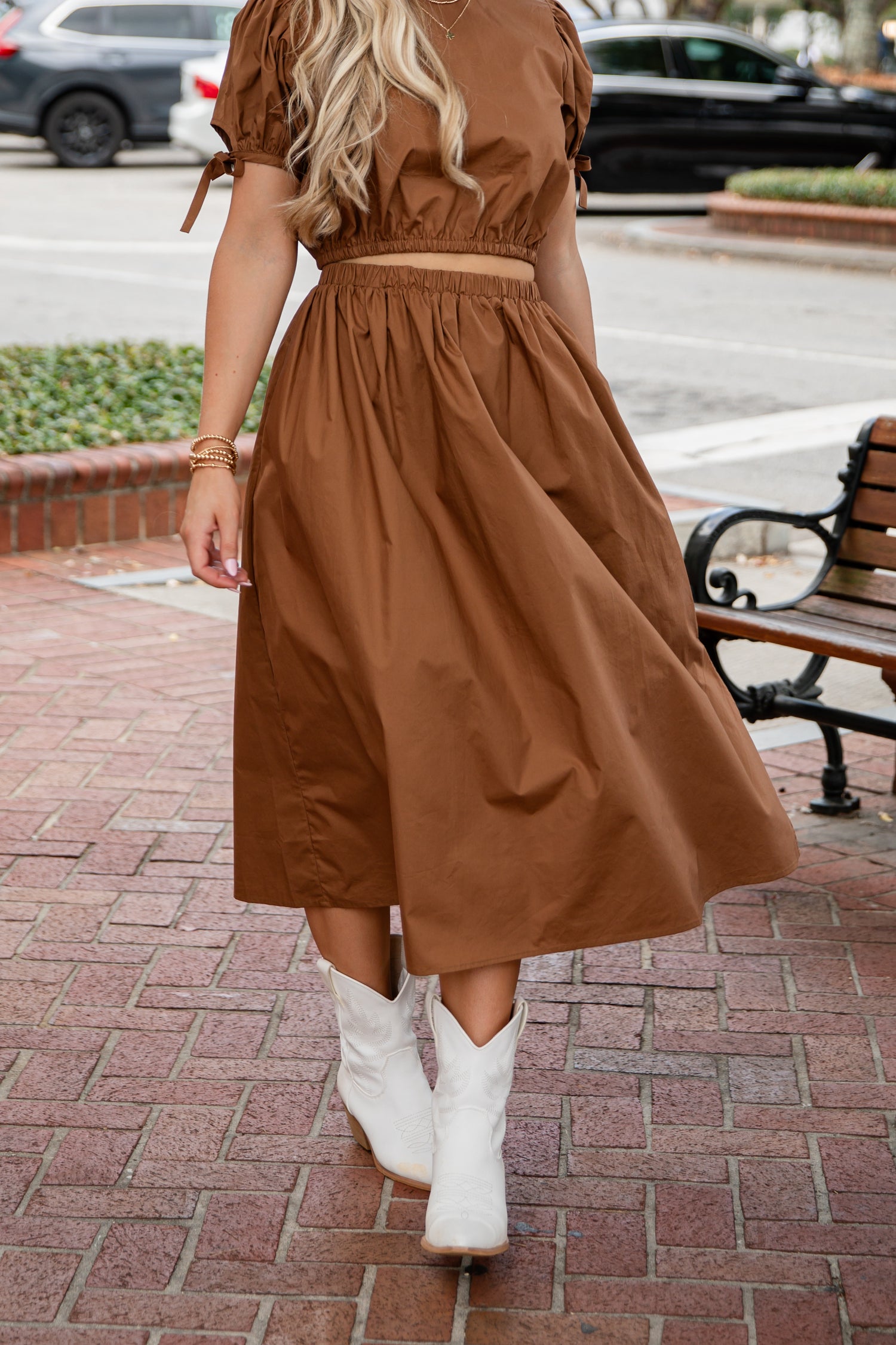 Woman in a brown dress and white boots walking on a sidewalk.