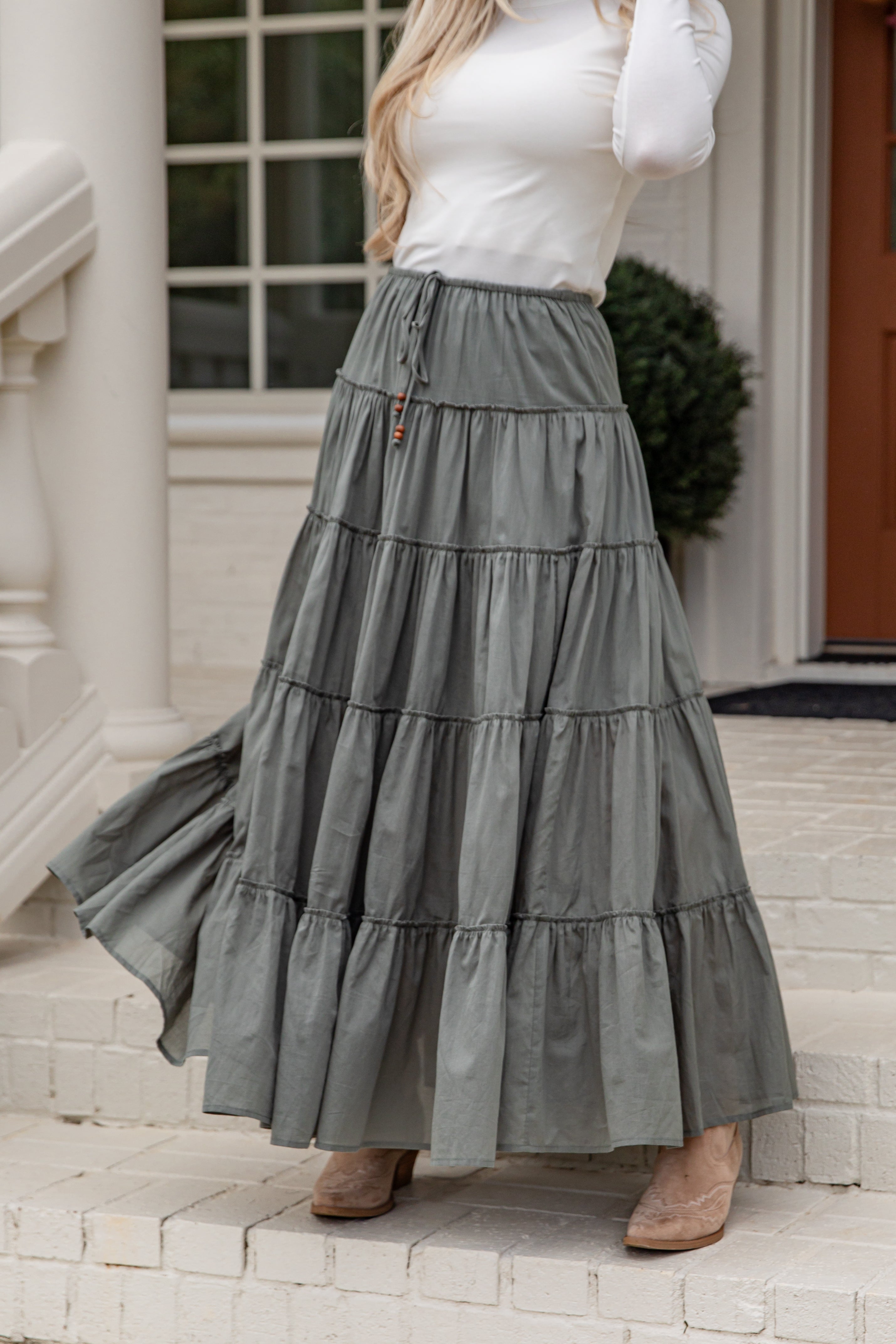 Woman wearing a long gray tiered skirt standing on steps outside a house.