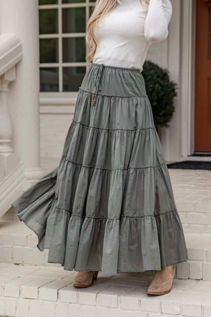 Woman wearing a long gray tiered skirt standing on steps outside a house.