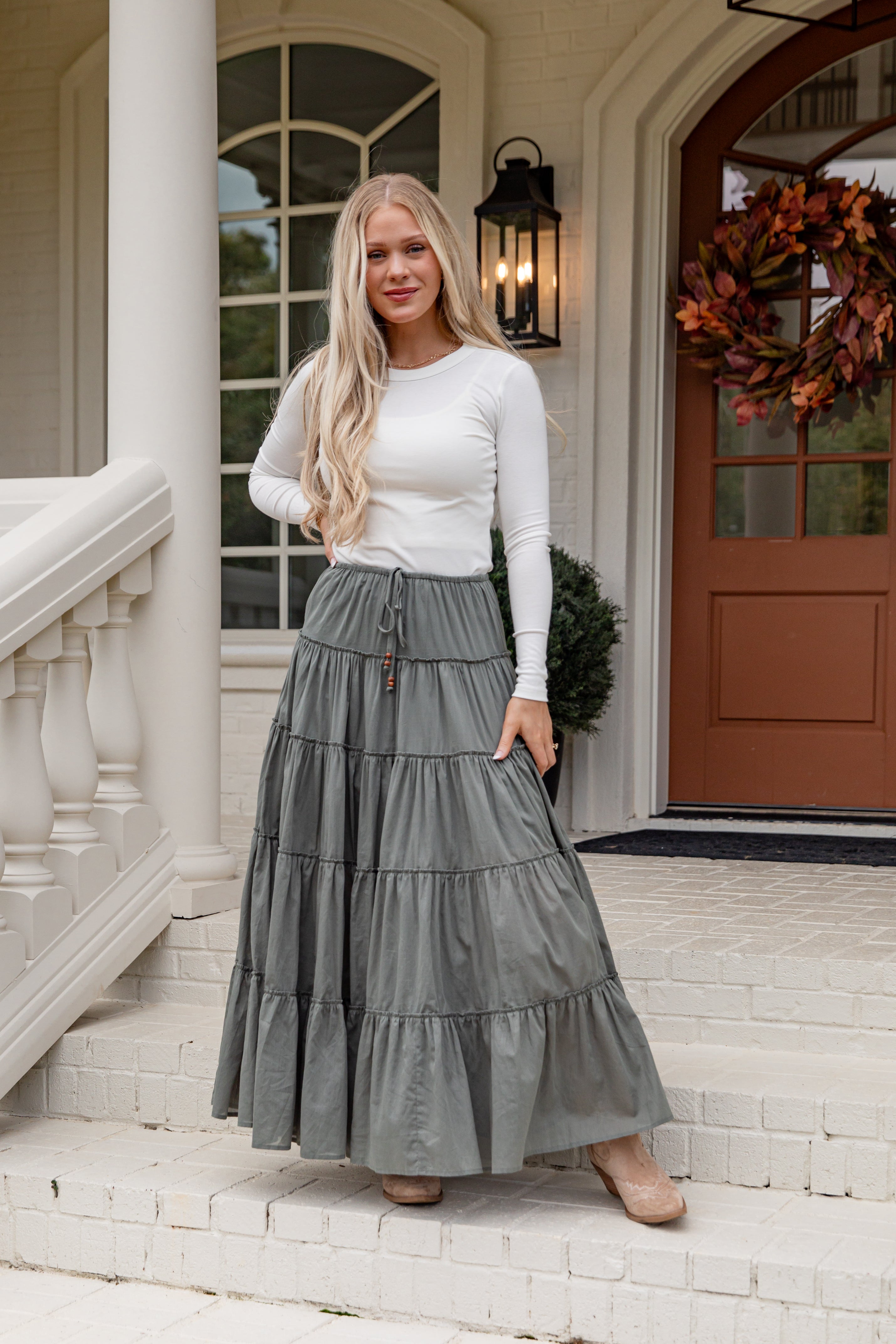 Woman in a white top and gray tiered skirt standing on a porch.