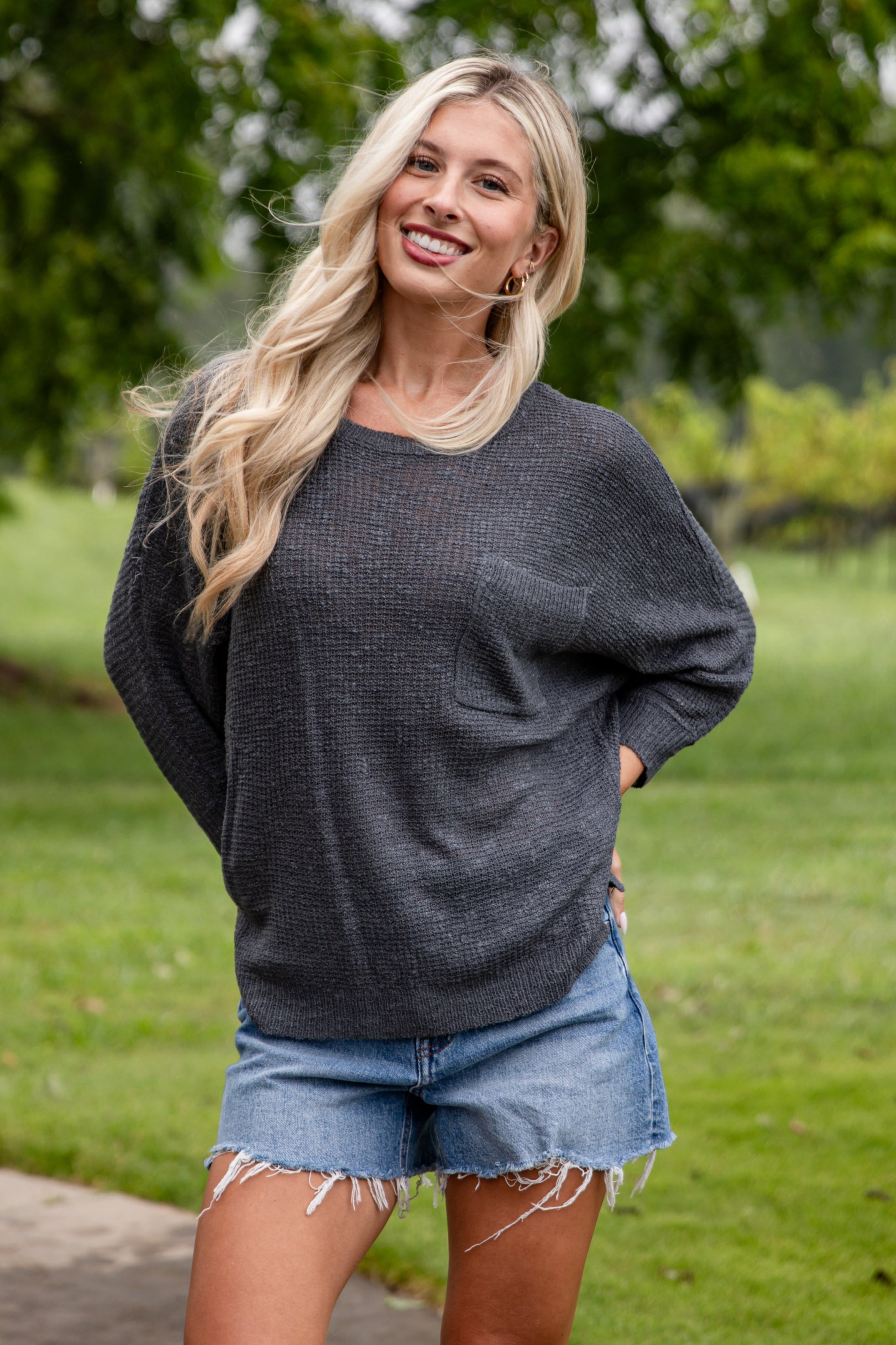 Woman standing outdoors in a casual setting with greenery