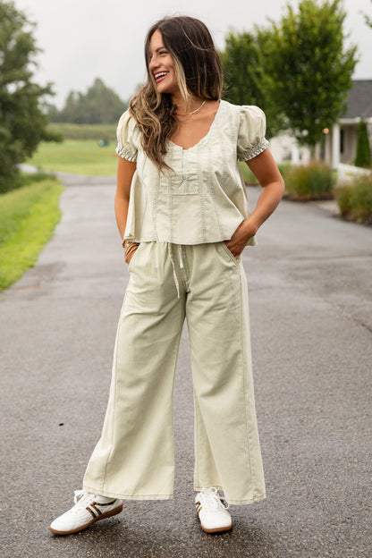 Woman in a light green outfit standing on a road with trees and a house in the background
