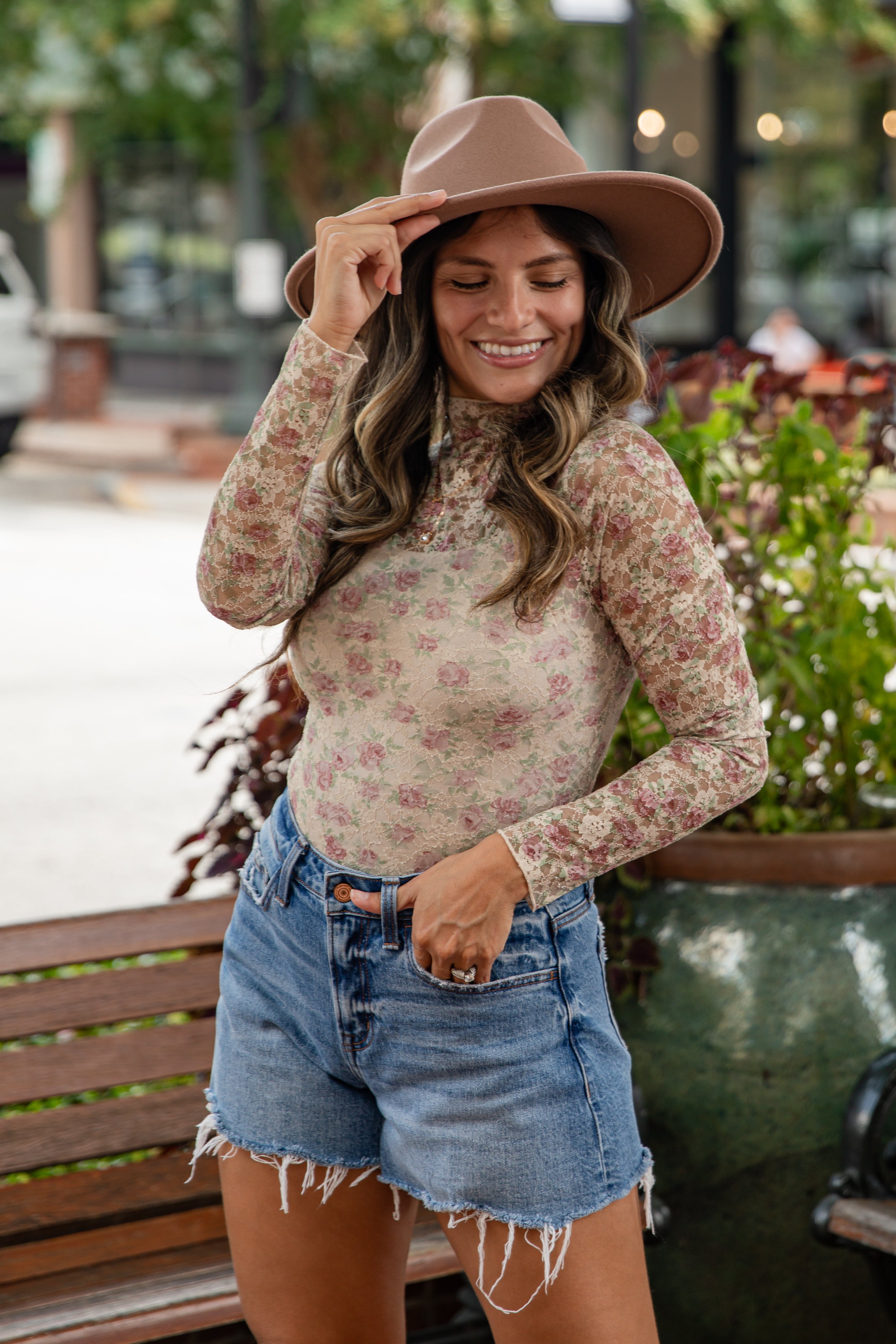 Woman wearing a floral top and denim shorts with a hat, standing outdoors.