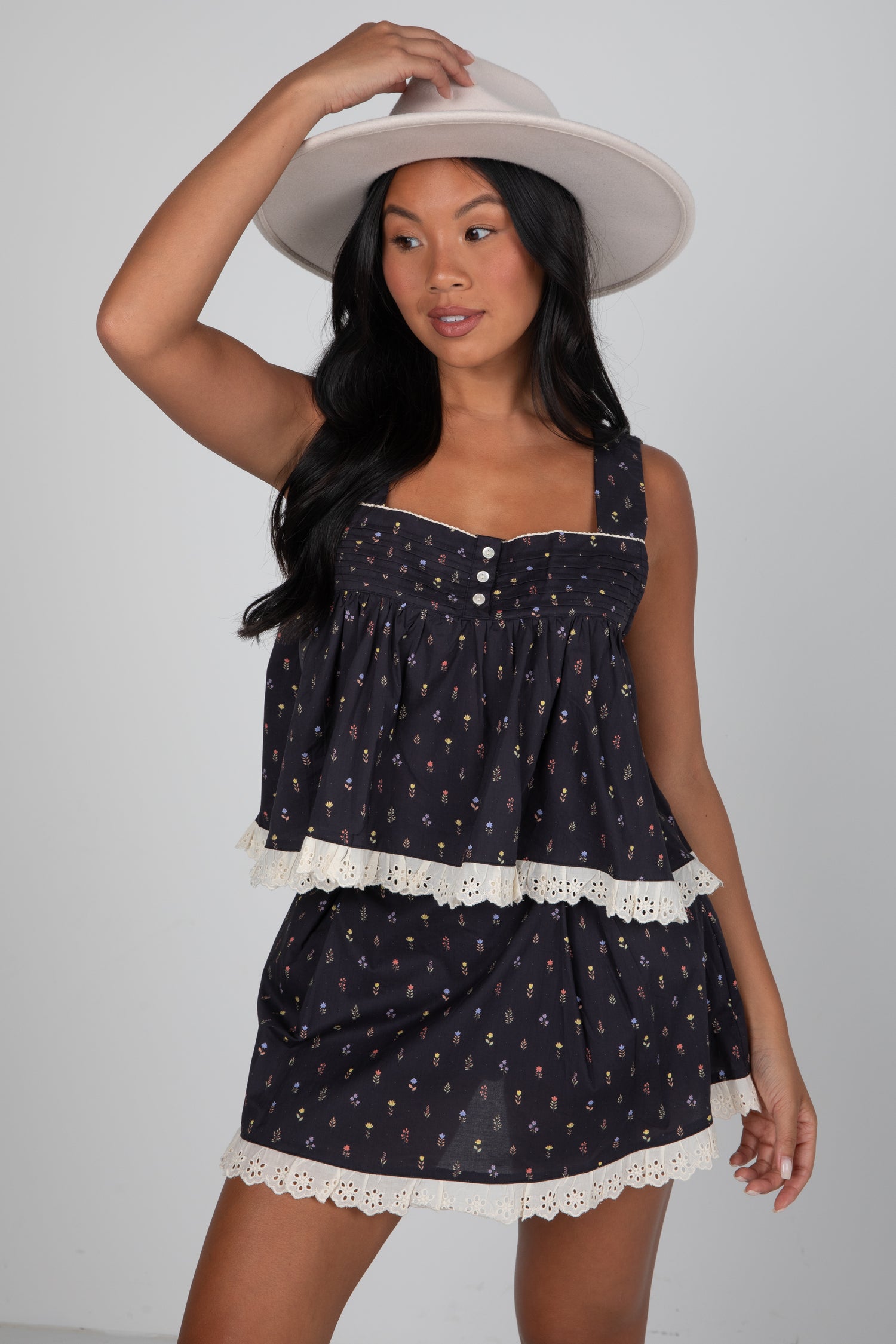 Woman wearing a black patterned dress with white lace trim and a white hat on a gray background