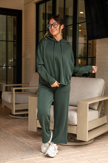 Woman wearing a green tracksuit standing outdoors near a patio chair.