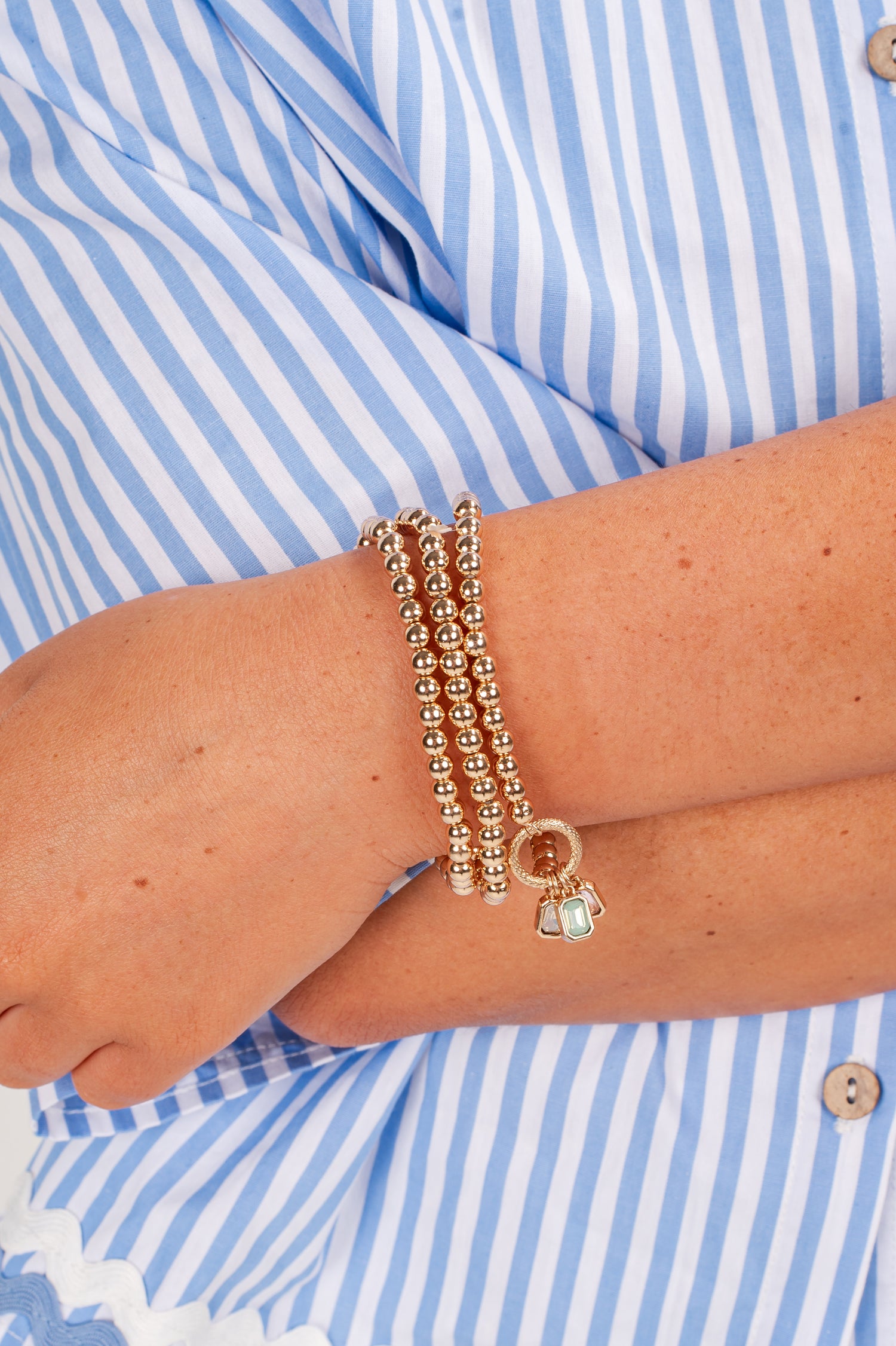 Gold bracelets on a wrist with a blue and white striped shirt
