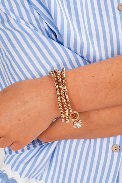 Gold bracelets on a wrist with a blue and white striped shirt