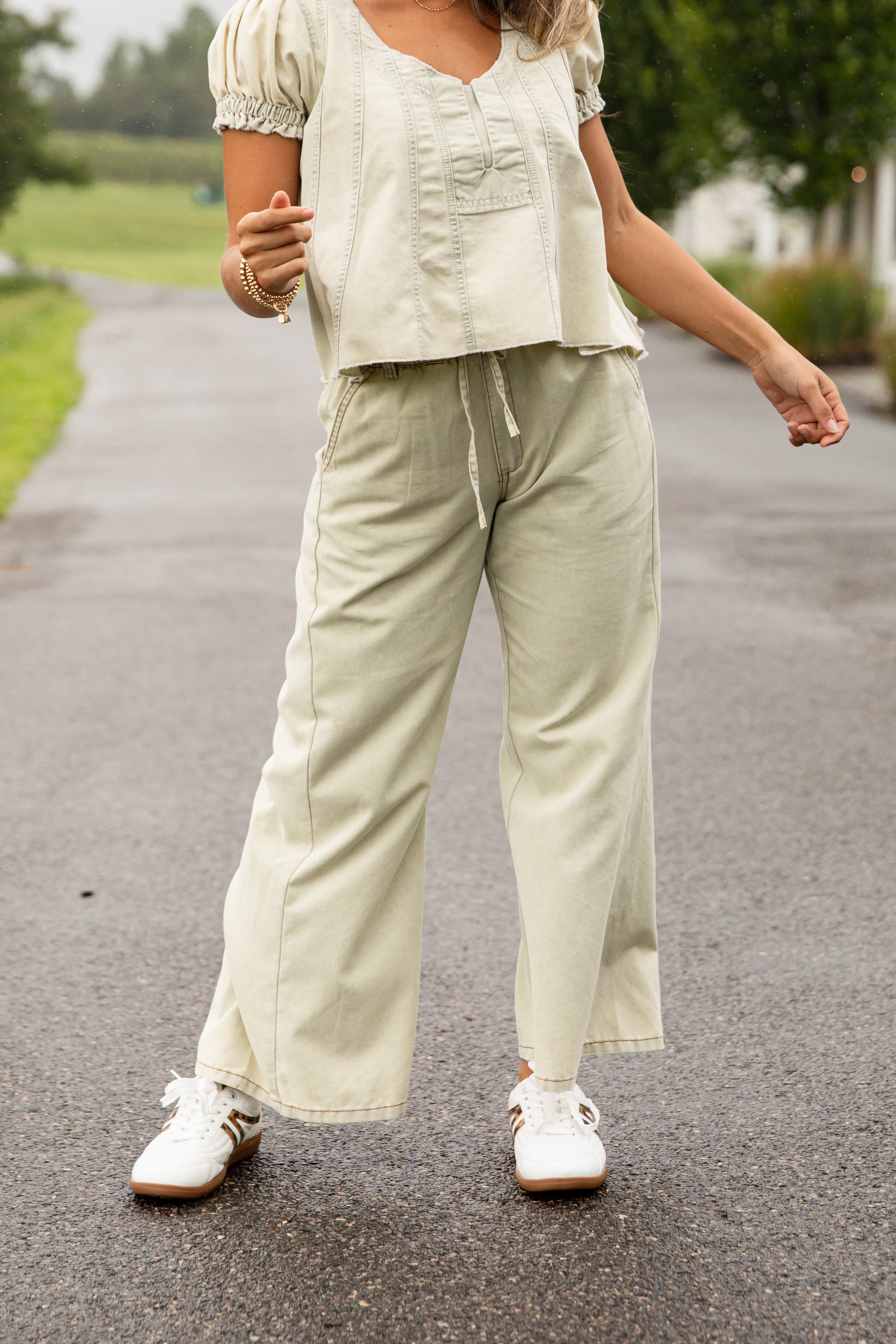 Person wearing a light green outfit with wide-leg pants and white shoes on a road.